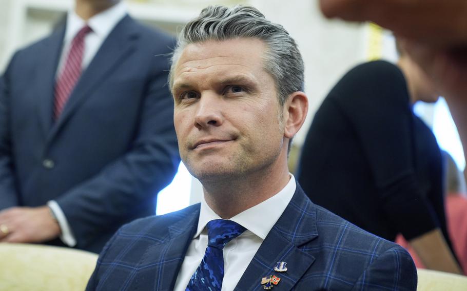 Close-up view of Pete Hegseth wearing a dark blue suit and tie seated on a couch.