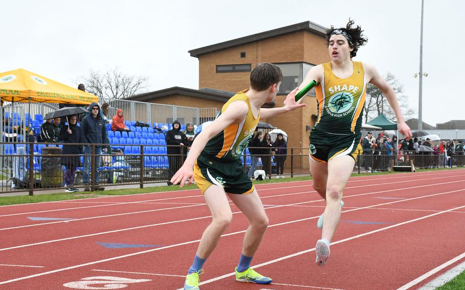 SHAPE senior Douglas Forbes hands off the baton to teammate David Van Wagenen to begin the final leg of the distance medley event Saturday, March 18, 2023 at RAF Lakenheath High School. 