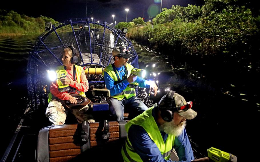 Donna Kalil, left, volunteer Dave Hackathorn, middle, piloting his airboat, and volunteer Dave Wagner hunt for pythons in the Everglades west of Weston, Fla., on Aug. 12, 2022. 