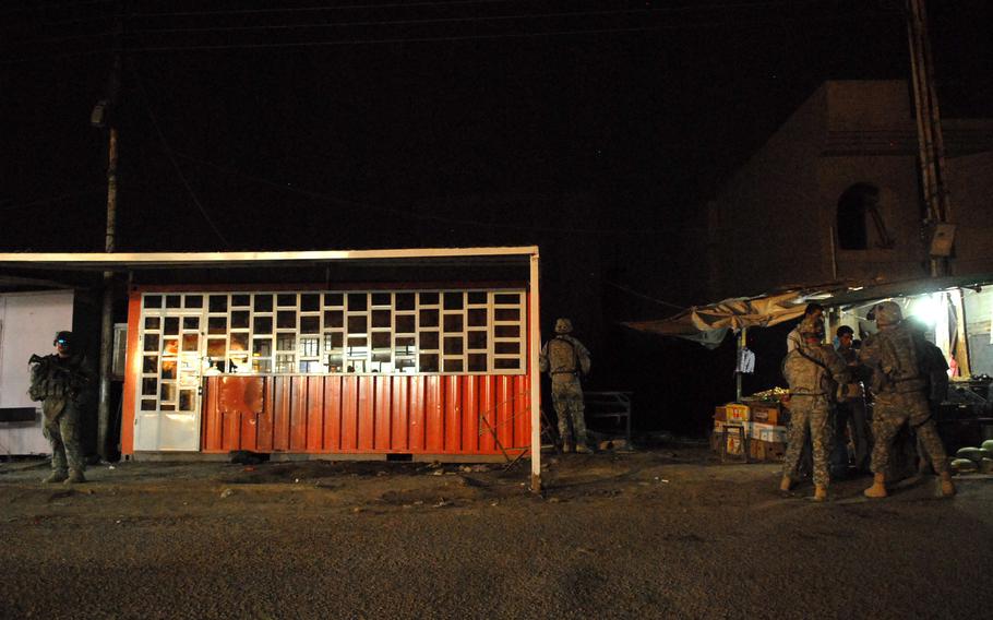 Soldiers from Troop A, 1st Battalion, 75th Cavalry Regiment talk to a produce vendor during a night patrol in western Baghdad.