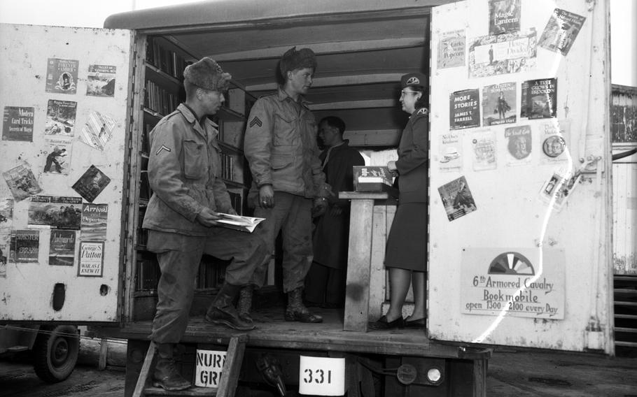 A black and white photo of service members talking to a woman in a truck full of books.