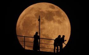 People are silhouetted as an almost full moon rises above the sky in Grozny, Russia, on Sunday, May 15, 2022.