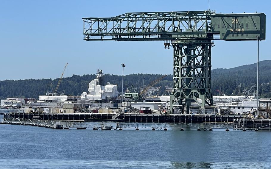 A large crane, seen from a distance, on the shore of a shipyard with water in the foreground.