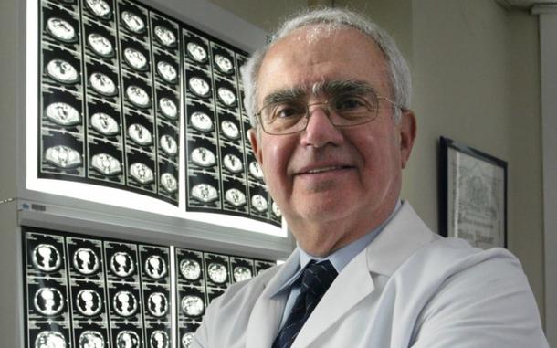 A doctor in a white coat poses for a photo in front of black and white medical images.