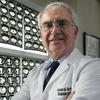 A doctor in a white coat poses for a photo in front of black and white medical images.