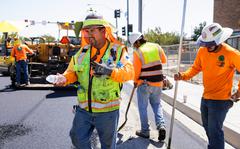 With temperatures over 100 degrees, construction worker Margarito Vargas from Eleven Western Builders gives fellow workers water bottles while paving a road in Livermore, Calif.