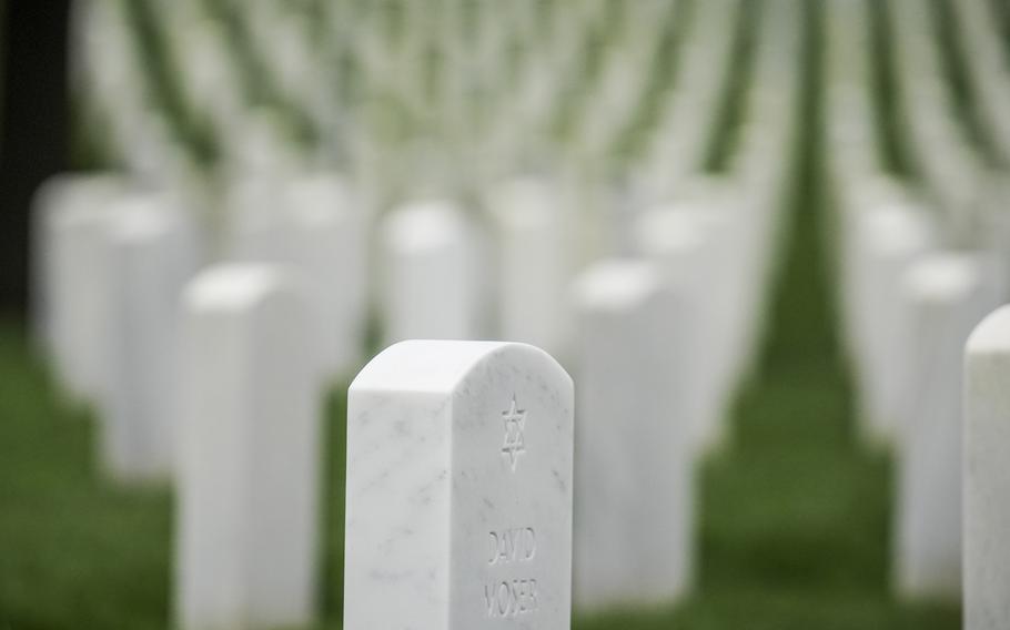 An in-focus tombstone with the Star of David engraved on it, while other tombstones are lined up out-of-focus behind it.