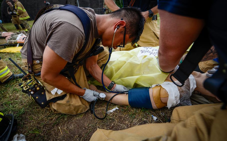 Senior Airman Philip Mathys, left, a firefighter with the 86th Civil Engineer Squadron takes a blood pressure measurement on a medical training mannequin at the scene of a simulated aircraft crash during Operation Varsity, a recurring emergency exercise at Ramstein Air Base, Germany, July 26, 2022. The mannequins provided first responders lifelike feedback, including vital signs, eye movement and audio responses.