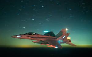A U.S. Navy F/A-18 Super Hornet flies against a dark greenish blue sky. 
