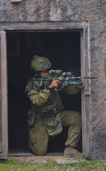 An Australian soldier kneels in a door frame at an urban combat training area at Bellows Air Force Base, Hawaii, July 18, 2022.