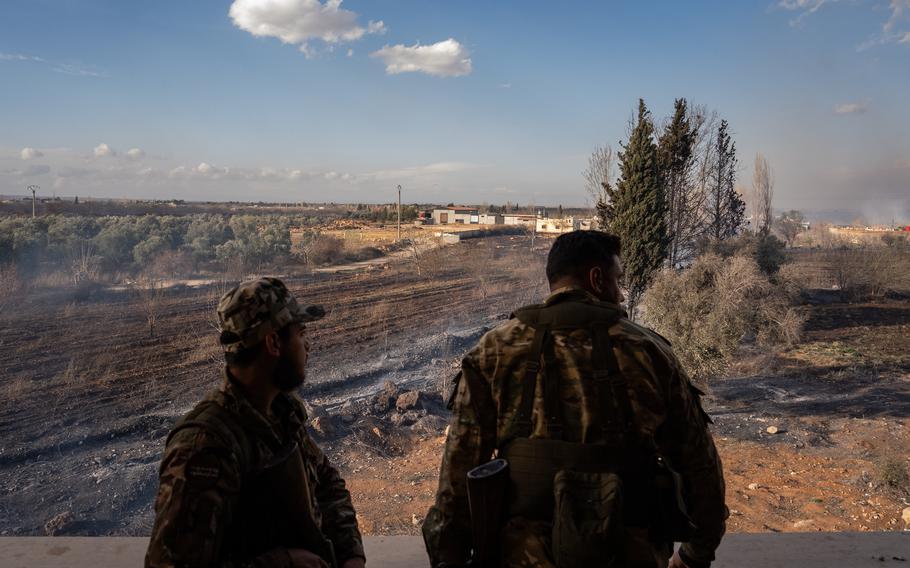 Two men in military uniforms overlook an expanse of land.