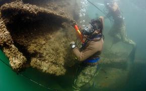 Two divers in scuba gear survey the wreckage of a ship under water.