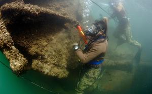Two divers in scuba gear survey the wreckage of a ship under water.