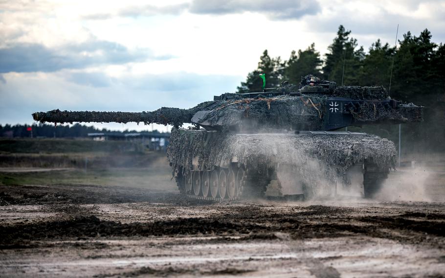 A German tank moves along a dirt road during an exercise with a treeline in the background.