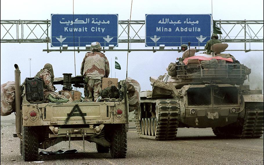 U.S. and Saudi military vehicles pass under a highway sign directing them to Kuwait City in February 1991 during Desert Storm Allied forces offensive. 