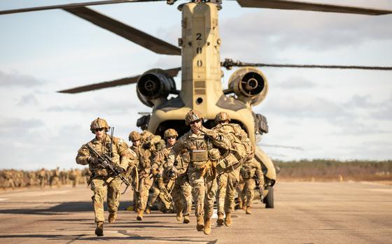 Soldiers in uniform wearing weapons run out of a helicopter. 