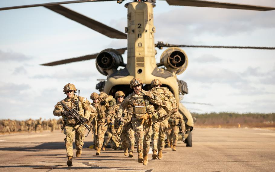 Soldiers in uniform wearing weapons run out of a helicopter. 