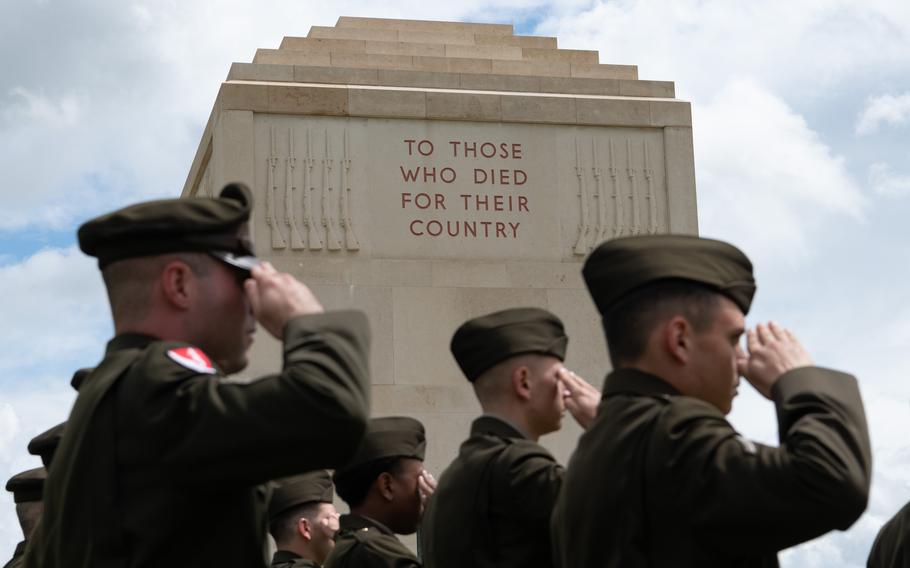 Four soldiers salute in front of the a memorial that says “To those who died for their country”