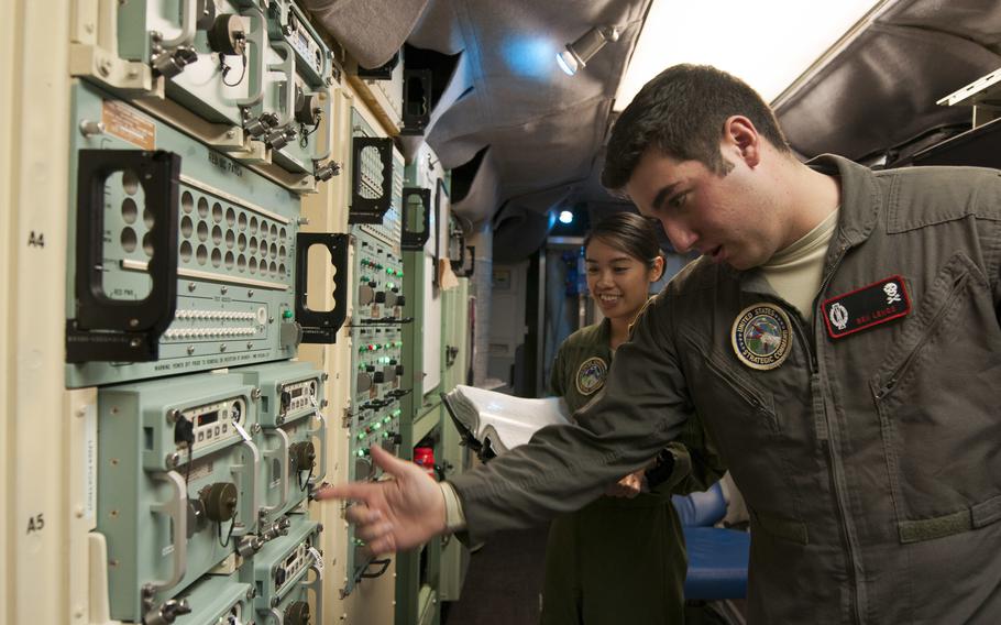 An airman flips a switch on a board while the other holds a book.
