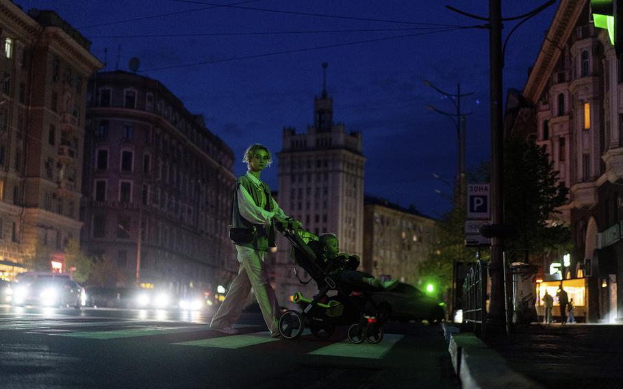 A woman pushes a cart carrying her child across a dark street after the municipality cut the city lights to conserve energy in Kharkiv, Ukraine, on April 14, 2024. 