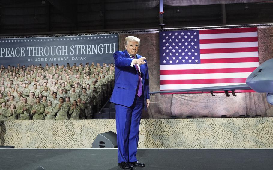 President Trump in a blue suit pointing a finger, with military personnel and the U.S. flag in the background.
