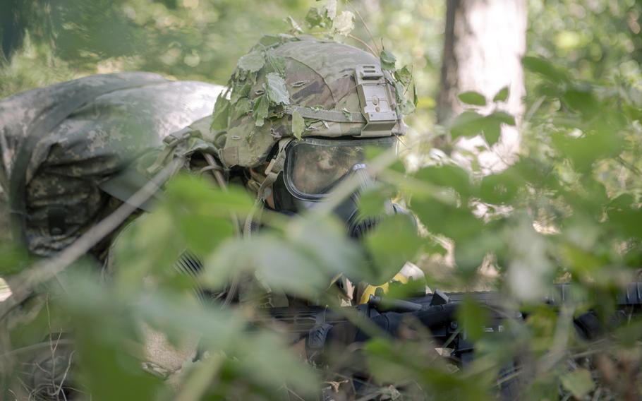 A soldier in full gear, with goggles, patrols in the woods.