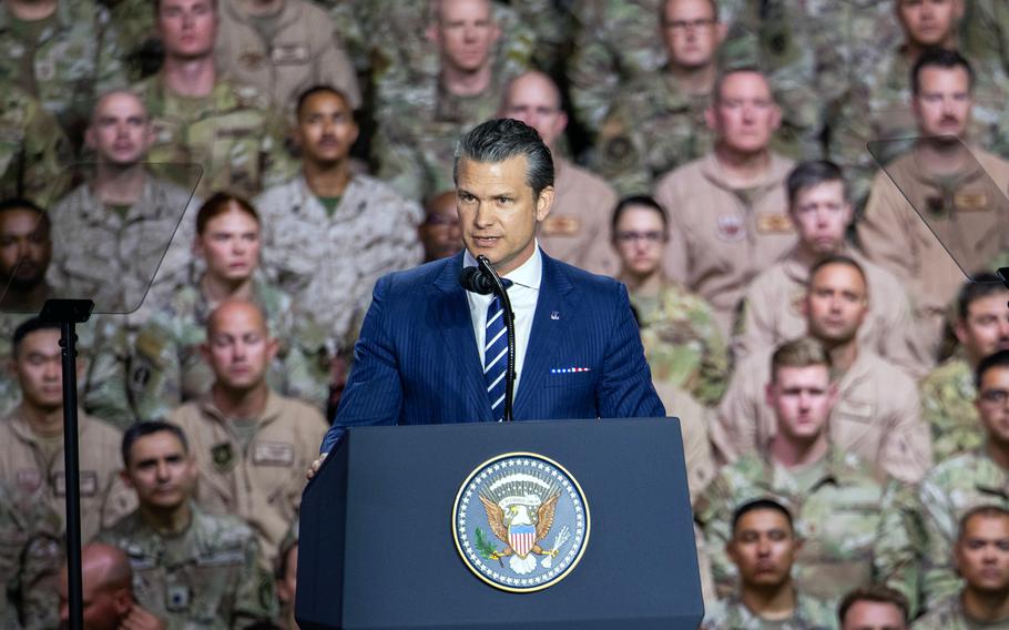 Hegseth speaks at the microphone with troops seated behind him.