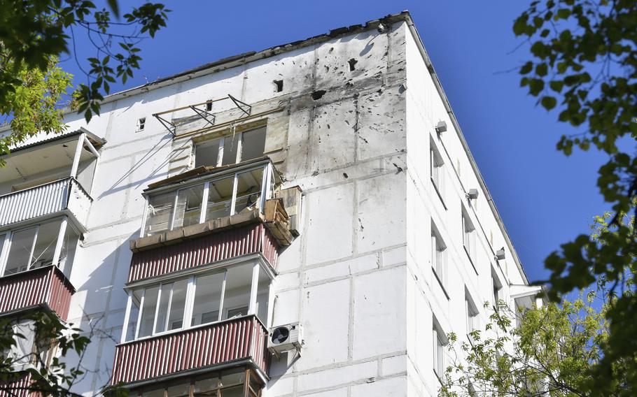 The top corner of a white apartment building against a blue sky, with part of a wall damaged.