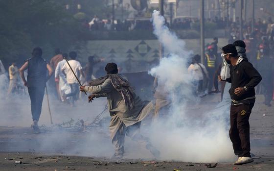 A supporter of former Prime Minister Imran Khan hurls back a tear gas shell fired by riot police officers to disperse them during clashes, in Lahore, Pakistan, Wednesday, March 15, 2023. Clashes between Pakistan's police and supporters of Khan continued outside his home in the eastern city of Lahore on Wednesday, a day after officers went to arrest him for failing to appear in court on graft charges.