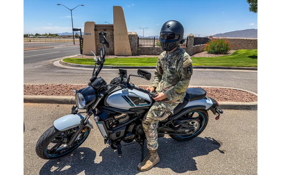 A soldier sits on a motorcycle with his helmet shield covering his face.