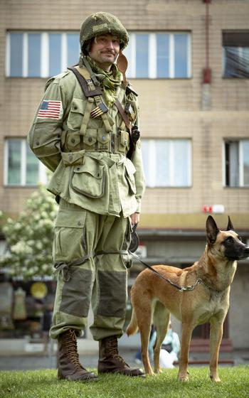 A man in uniform stands with his dog.