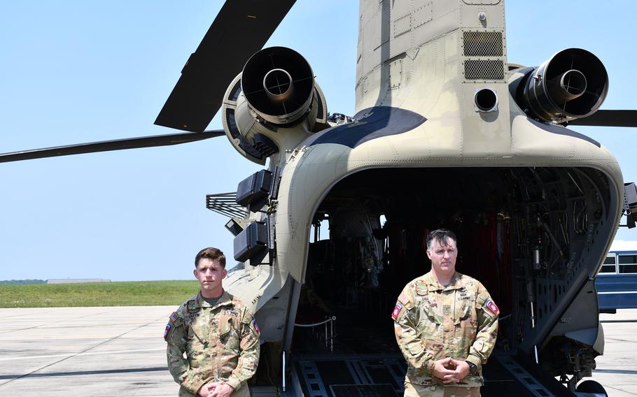 Two male soldiers stand outside a helicopter.