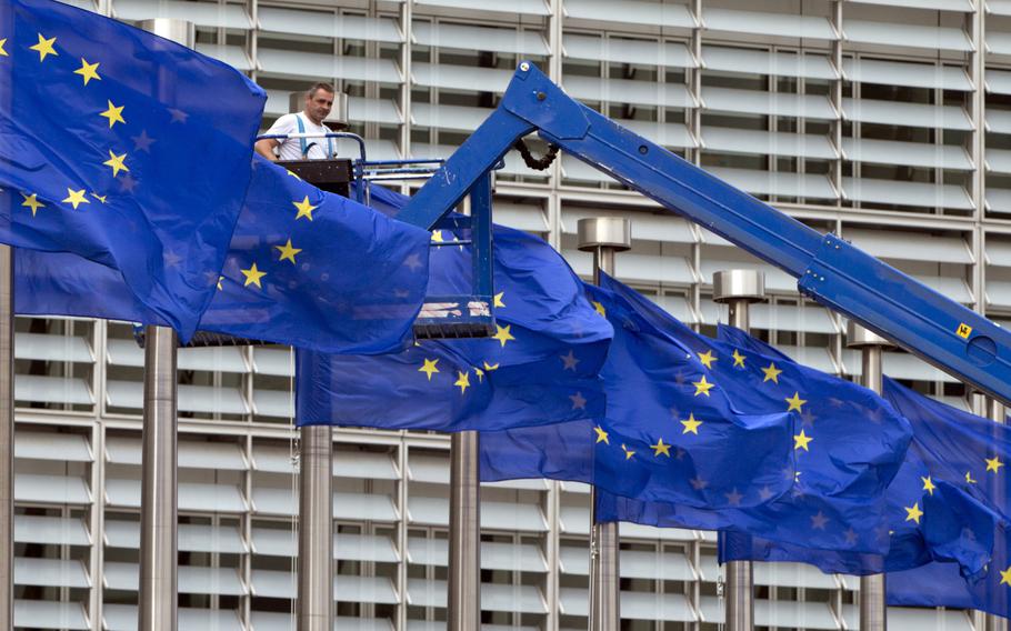 FILE- In this June 23, 2016 file photo, a worker on a lift adjusts the EU flags in front of EU headquarters in Brussels. The European Union’s enlargement policy is at an impasse as its leaders gather for a summit focused on how to deal with Western Balkans neighbors that have been trying to enter the club for two decades. Meanwhile, the region is increasingly getting support from China and Russia instead.