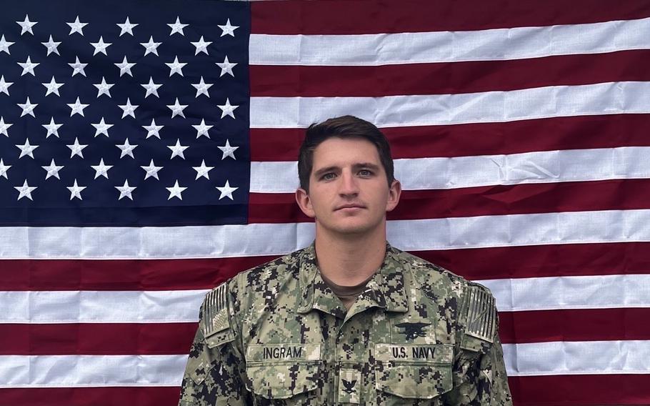 A young man in uniform seen from the chest up against the American flag.