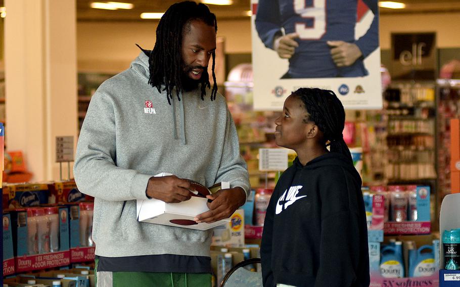 Kalani Morgan, left, listens to New England Patriot outside linebacker Matthew Judon as he signs a football duirng an autograph event on March 23, 2024, at the Kaiserslautern Military Community Center on Ramstein Air Base, Germany.