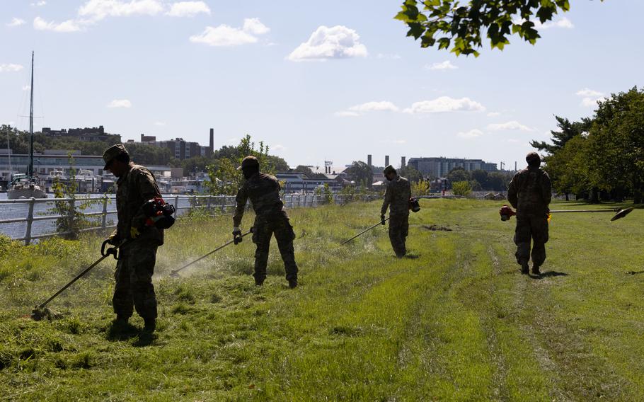 Soldiers cutting grass on a lawn near a river.
