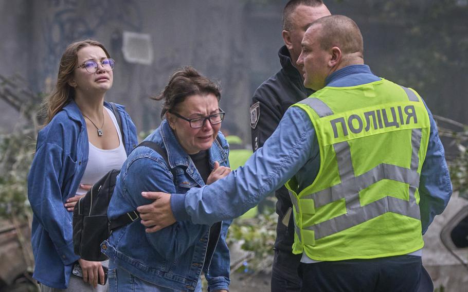 Ukrainians mourn while emergency workers hold their arms.