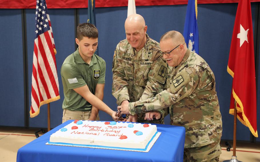 New York Army National Guard Pvt. Sean McCauley, age 17, joins Chief Warrant Officer 5 Mark Shumway, the New York Army National Guard command chief warrant officer, and Chief Warrant Officer 5 Michael Zanghi, age 60, in cutting the National Guard birthday cake during a ceremony marking the 387th anniversary of the National Guard on Dec. 13, 2023, at New York National Guard headquarters in Latham, N.Y. McCauley, who enlisted in July and was the youngest Guardsman present, represented the future of the National Guard, while Zanghi, who retires in February 2024 represented the history and traditions of the Guard. Shumway served as the presiding officer for the ceremony.