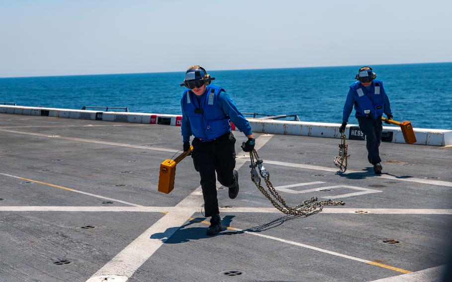 Two sailors run on the deck of a ship while carrying equipment.