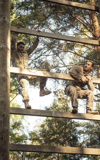 A vertical photo of two soldiers climbing a ladder-like obstacle.