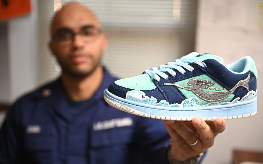 Petty Officer 2nd Class Kenneth Jones presents his own custom created sneaker from an online competition in Norfolk, Va., Nov. 29, 2023. Jones’ custom sneaker represents the ocean, including the famous Statue of Neptune from Virginia Beach. Inside of the tongue is printed “By VA 4 VA Thank You” as his final appreciation to anyone that owns the sneaker and represents for the area.