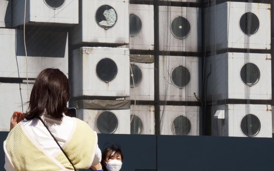 A woman poses for a photo in front of Nakagin Capsule Tower in Tokyo's Ginza district, Tuesday, April 12, 2022. 