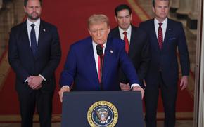 Donald Trump stands at a podium and speaks into a microphone while JD Vance, Marco Rubio and Pete Hegseth stand behind him on a red carpet.