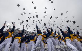 A ground-level shot of Air Force Academy graduates in uniform and throwing their caps into the air to celebrate graduating.