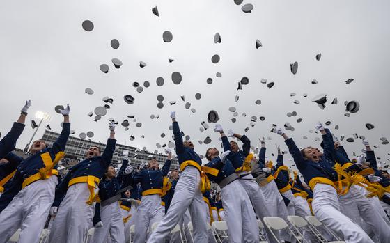 A ground-level shot of Air Force Academy graduates in uniform and throwing their caps into the air to celebrate graduating.