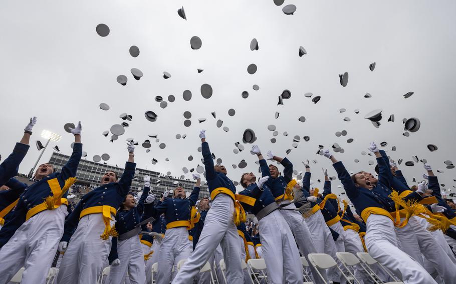 A ground-level shot of Air Force Academy graduates in uniform and throwing their caps into the air to celebrate graduating.