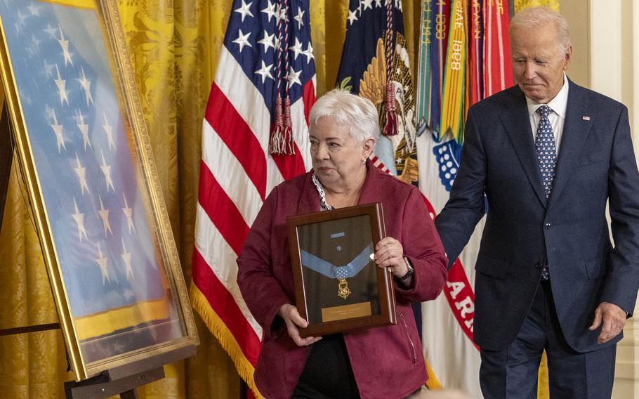 An elderly woman holds a framed Medal of Honor awarded posthumously to her father while standing next to Joe Biden.