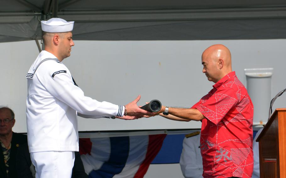 Ken Inouye, son of the late Hawaiian Sen. Daniel Inouye, passes the long glass to a sailor during the commissioning of the USS Daniel Inouye at Joint Base Pearl Harbor-Hickam, Hawaii, Dec. 8, 2021. The pass is part of a tradition to signify the start of the first watch.