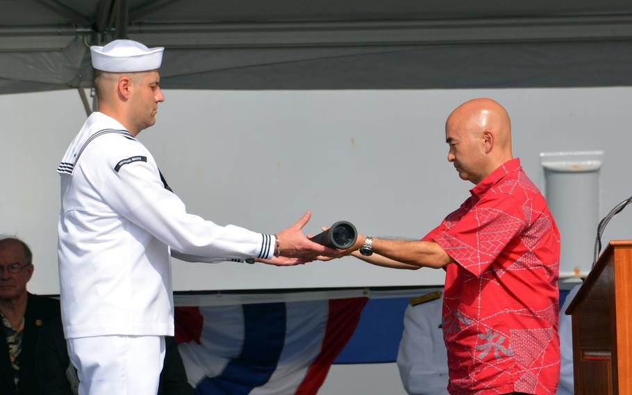 Ken Inouye, son of the late Hawaiian Sen. Daniel Inouye, passes the long glass to a sailor during the commissioning of the USS Daniel Inouye at Joint Base Pearl Harbor-Hickam, Hawaii, Dec. 8, 2021. The pass is part of a tradition to signify the start of the first watch.