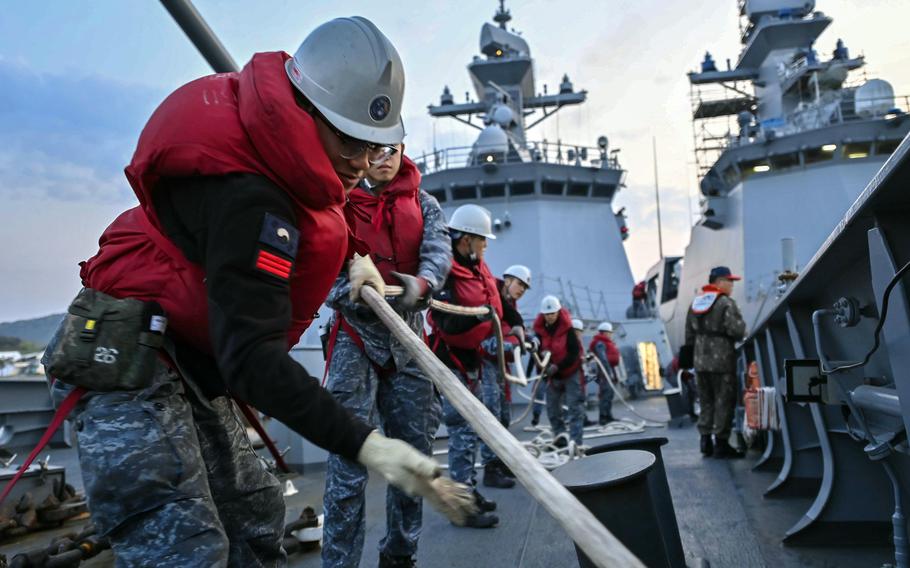 South Korean sailors in orange safety vests pull on a rope to prepare to depart for an exercise.